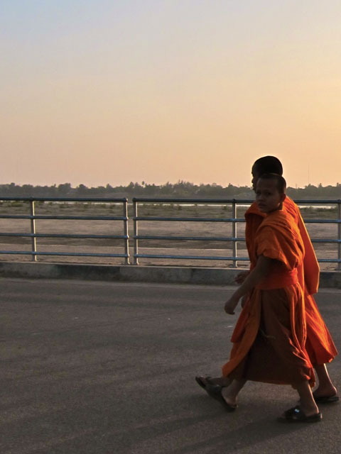 Monks walking on a sidewalk alongside a river